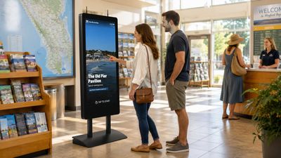 A couple explores local attractions on a HootBoard AirX kiosk in a busy visitor center
