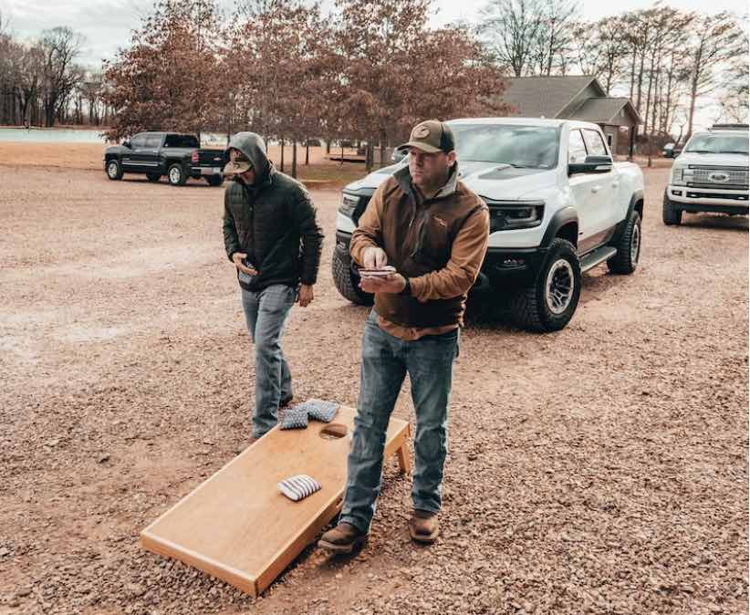 two guys playing cornhole outside next to a truck